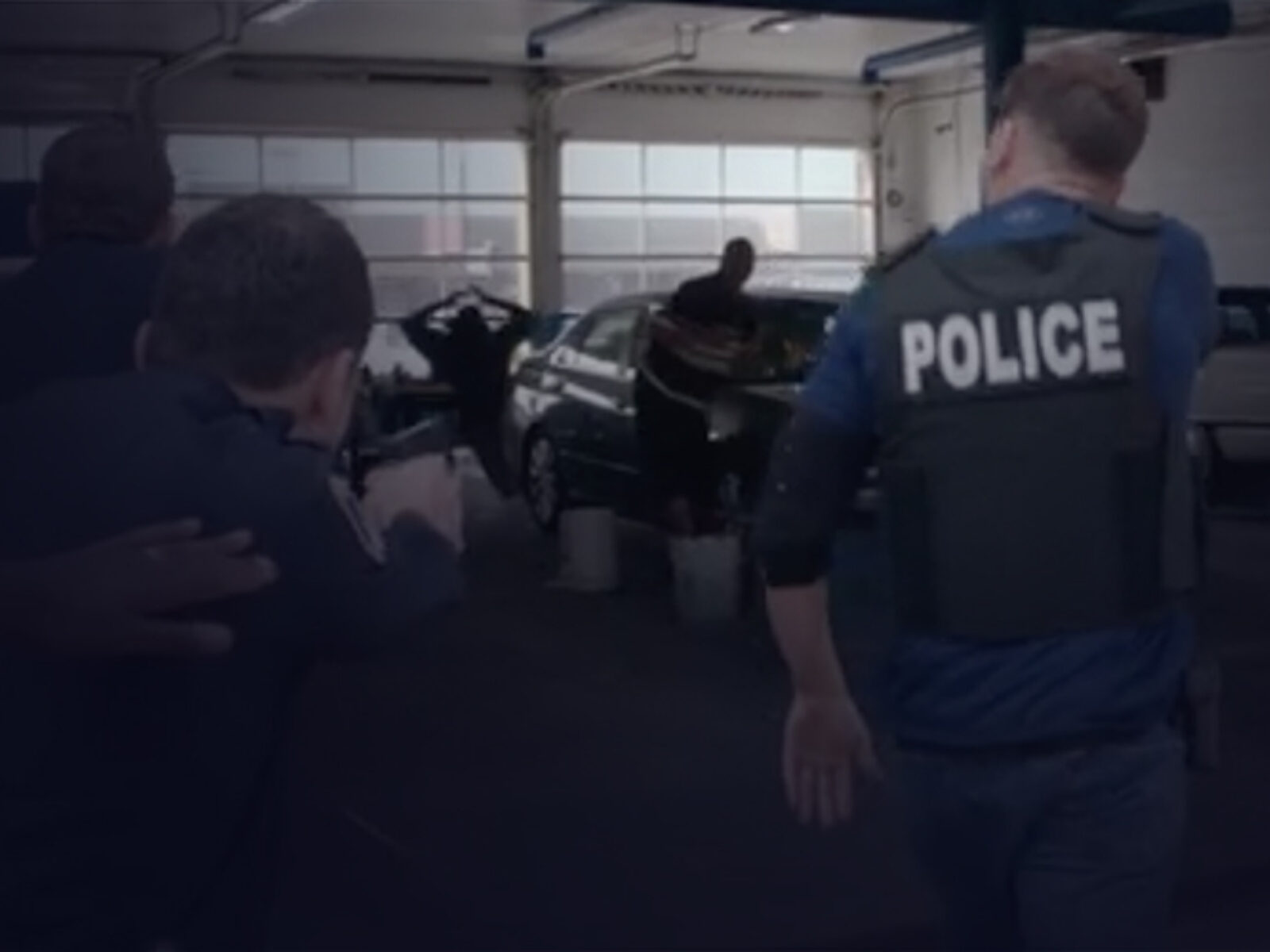 3 police officers from the back, pointing their guns to 2 people surrendering