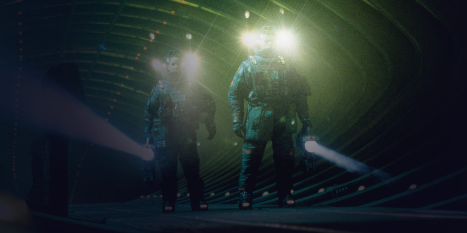Two astronauts in a large indoor space, each holding a big flashlight