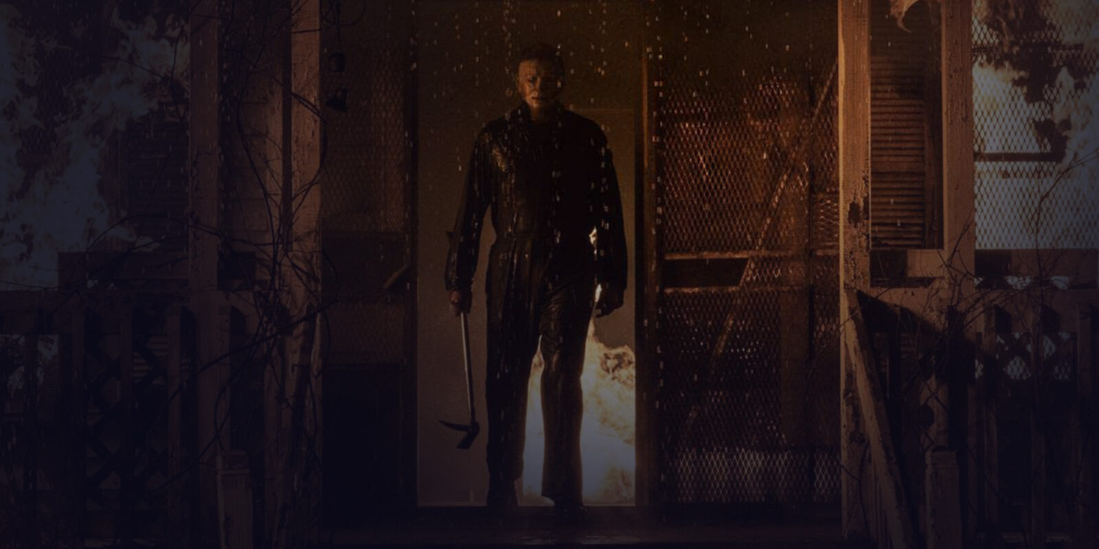 Man in a mask walking out of a burning building with an ax in his hand