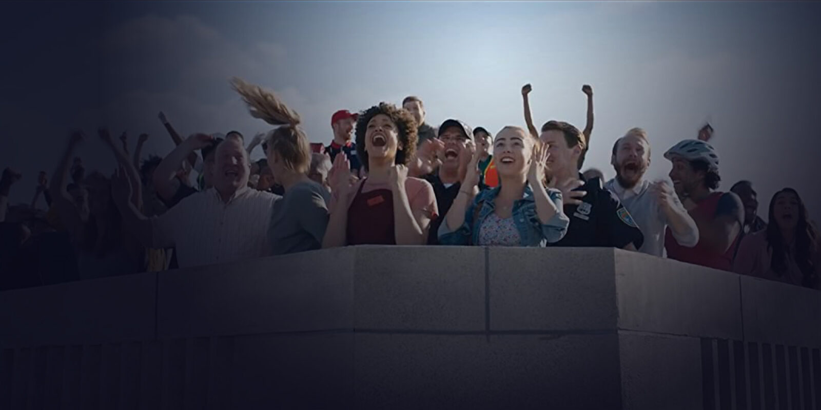 A large group of people on top of a building smiling, with their hands in the hair and celebrating.