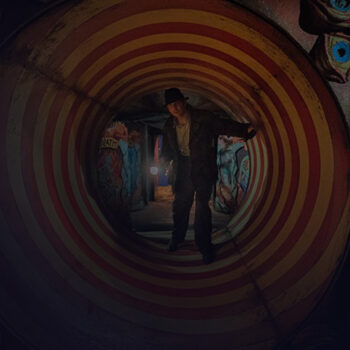 Man holding a flashlight standing on a tunnel with stripes, surrounded by fake eyes