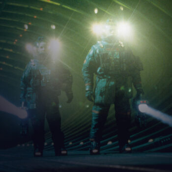 Two astronauts in a large indoor space, each holding a big flashlight
