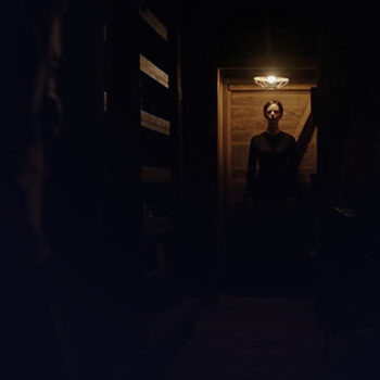 Long shot of a woman standing in the dark under a ceiling light
