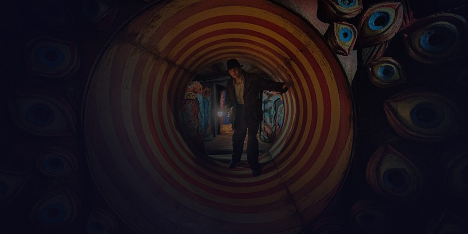 Man holding a flashlight standing on a tunnel with stripes, surrounded by fake eyes