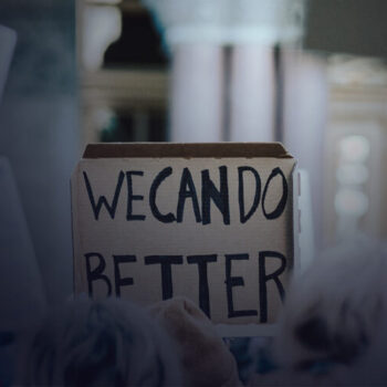 Hands holding a handwritten sign saying "We can do better"