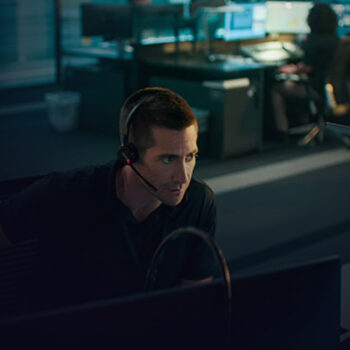 Man with wireless headphones sitting at a desk and looking at two computer screens.